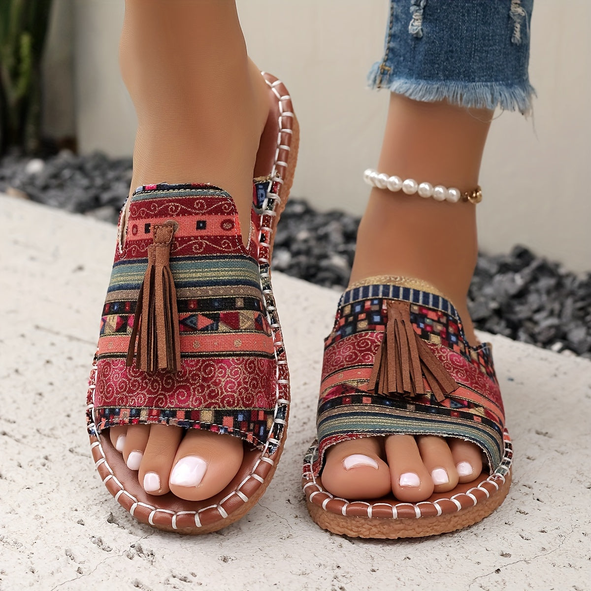 Sandales bohèmes colorées avec motifs ethniques et pompons, portées avec un jean déchiré et un bracelet de cheville perlé. Mode estivale tendance.