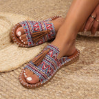 Sandales bohèmes colorées avec motifs géométriques et pompons, portées sur un tapis en paille. Chaussures d'été tendance pour femmes.
