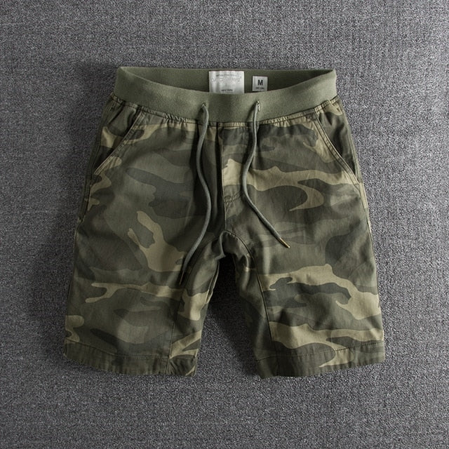 Short en tissu camouflage vert pour homme, taille moyenne, avec cordon de serrage, sur fond gris. Mode décontractée, style militaire.