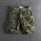 Short en tissu camouflage vert pour homme, taille moyenne, avec cordon de serrage, sur fond gris. Mode décontractée, style militaire.