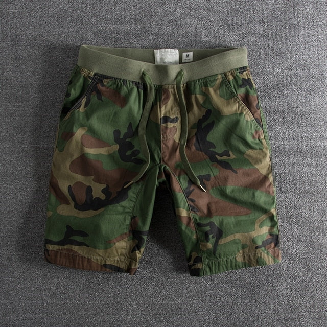Short en tissu camouflage vert et marron pour homme, taille M, sur fond gris. Mode décontractée, style militaire, vêtement estival.