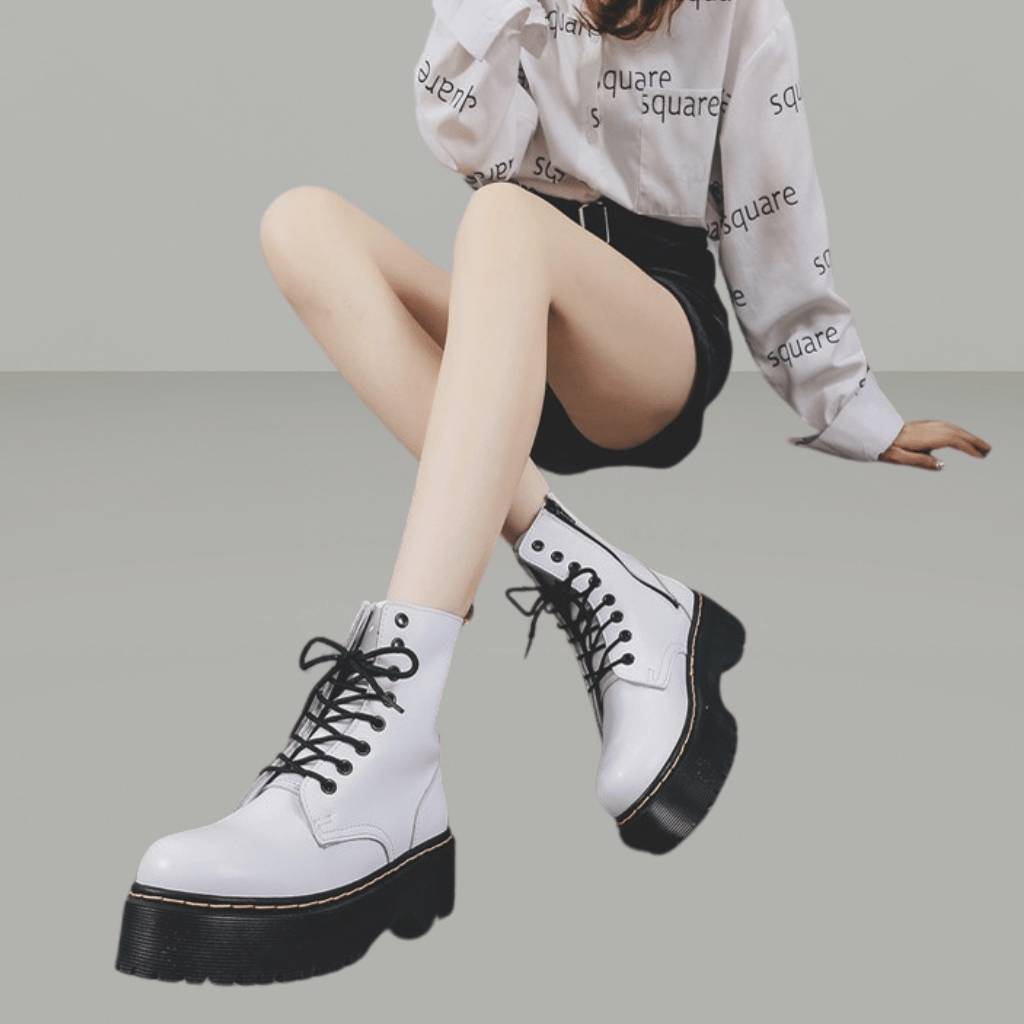 Femme portant des bottes blanches à plateforme avec lacets noirs, chemise imprimée "square", et short noir. Mode urbaine, style moderne.