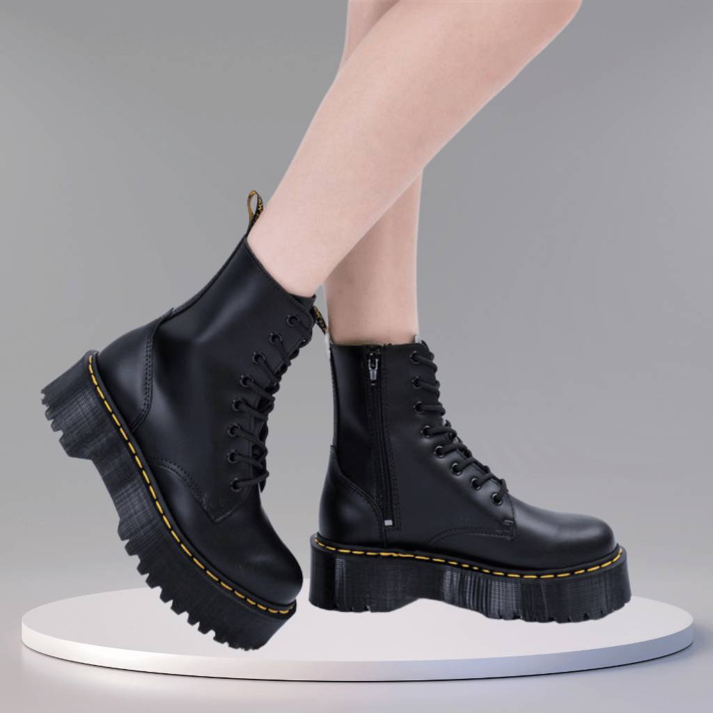 Bottes noires à plateforme épaisse, style combat, avec lacets et fermeture éclair, posées sur un fond gris. Mode tendance, chaussures femme.