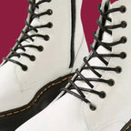 Bottes blanches en cuir avec lacets noirs sur fond bordeaux. Chaussures tendance, style punk, semelle épaisse. Mode urbaine, look moderne.
