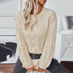 Femme portant un pull en tricot beige avec motif torsadé, posant dans un intérieur moderne. Mode automne-hiver, style décontracté chic.