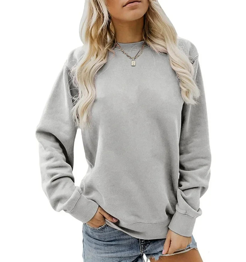 Femme portant un sweat-shirt gris ample et un short en jean, cheveux blonds ondulés, collier doré, style décontracté, mode féminine tendance.