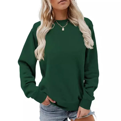 Femme portant un pull vert foncé, manches longues, col rond, avec un collier doré, associée à un short en jean. Mode décontractée tendance.