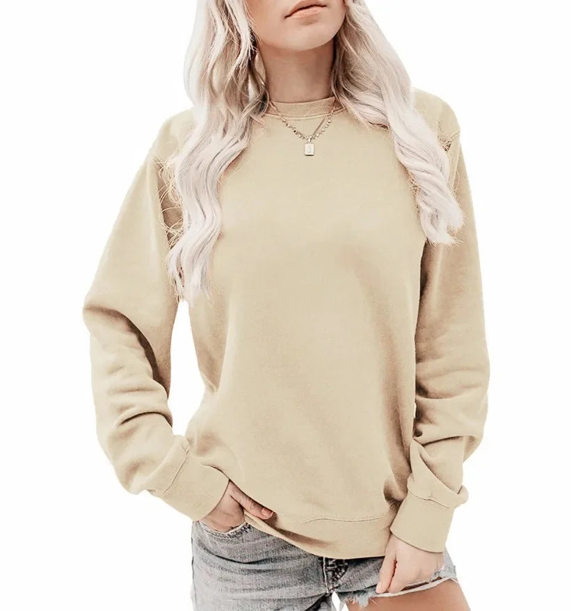 Femme en pull beige à manches longues, cheveux blonds ondulés, portant un collier, associée à un short en jean. Mode décontractée tendance.