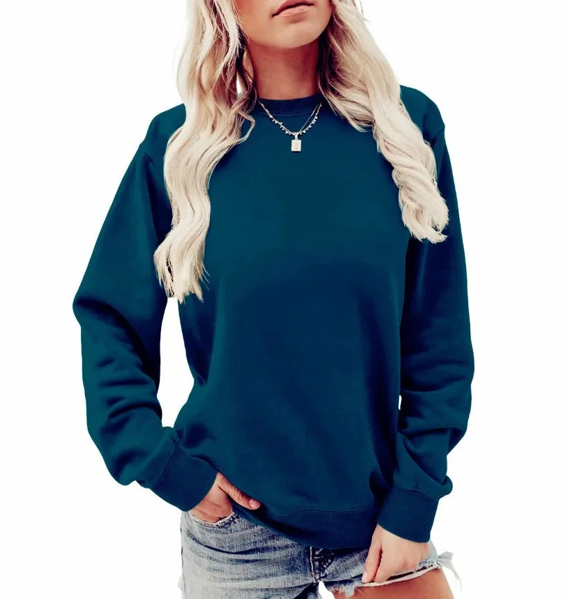 Femme en sweat-shirt bleu marine, manches longues, col rond, portant un collier argenté, cheveux blonds ondulés, tenue décontractée, fond blanc.