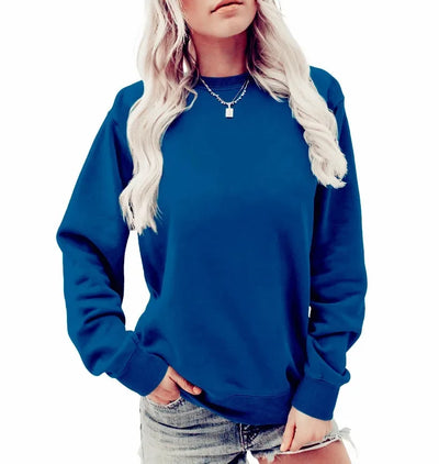 Femme portant un sweat-shirt bleu uni, manches longues, col rond, avec un collier argenté, posant en jean court. Mode décontractée tendance.