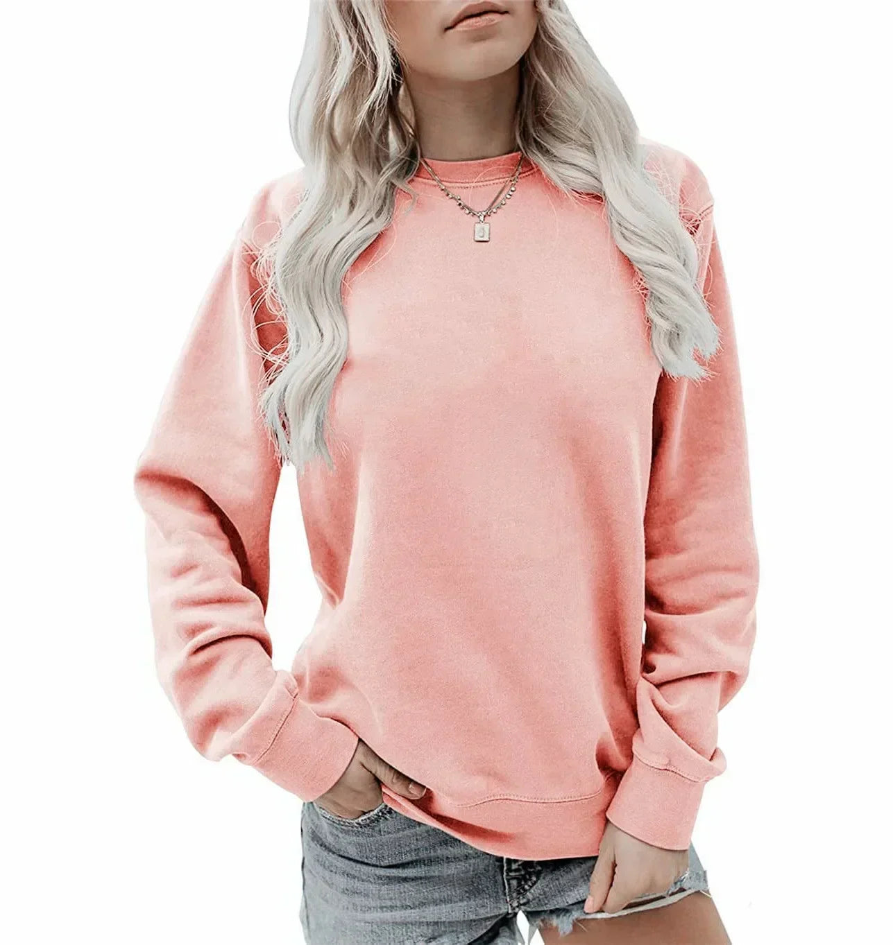Femme portant un pull rose pastel, manches longues, col rond, avec un collier argenté, et un short en jean. Mode décontractée féminine.
