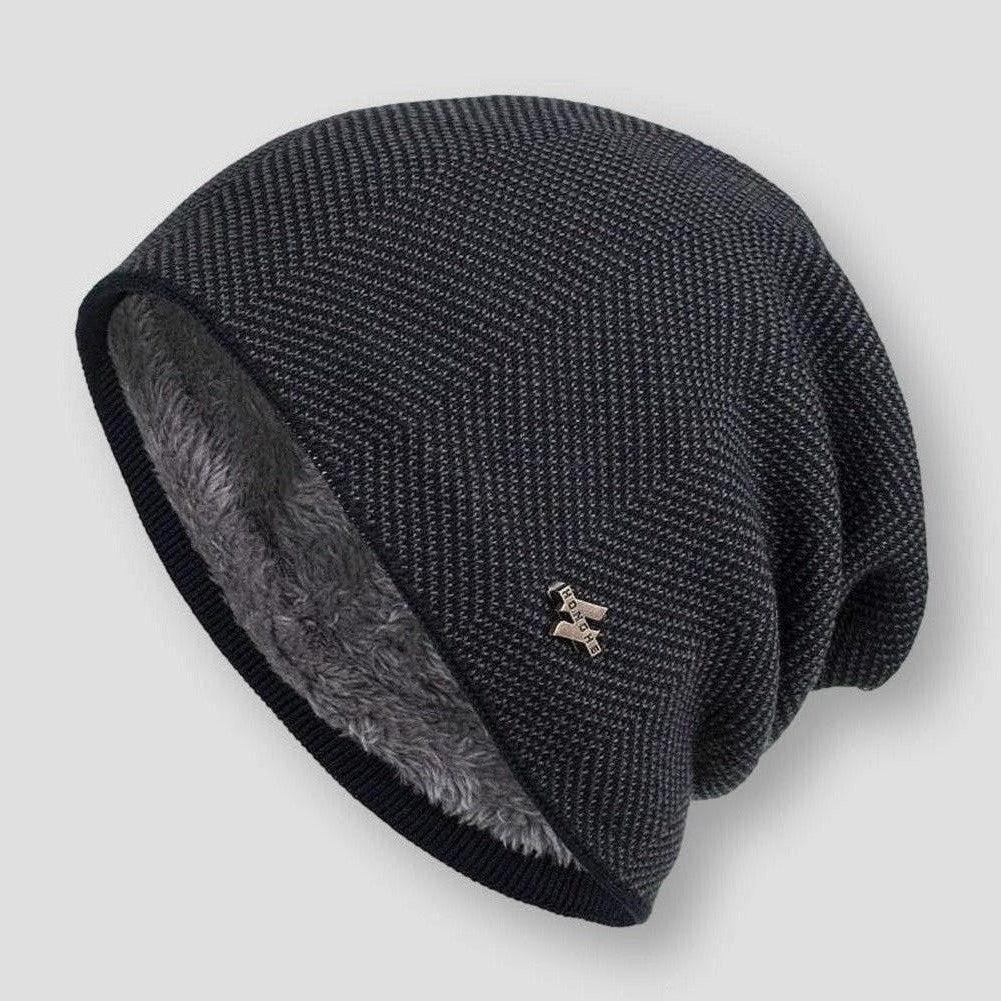 Bonnet en laine noir avec doublure en fourrure grise, motif chevrons, et broche métallique. Accessoire hiver tendance et chaud.