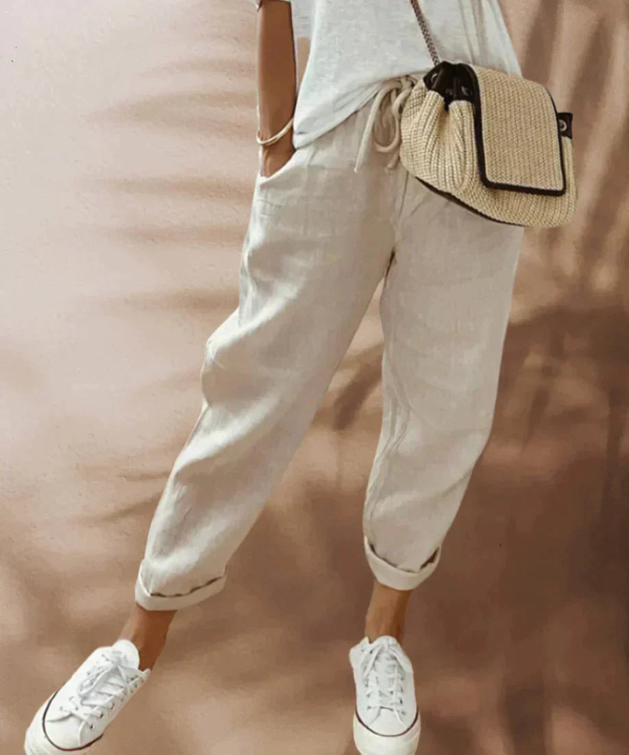 Pantalon en lin beige décontracté pour femme, associé à un t-shirt blanc et un sac en osier, style estival chic. Mode féminine tendance.