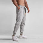 Homme portant un pantalon de jogging gris, style décontracté, avec baskets blanches. Mode masculine, confort, vêtements de sport tendance.