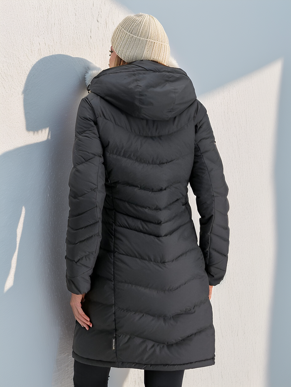 Femme portant un manteau d'hiver noir matelassé avec capuche, vue de dos, contre un mur blanc. Mode hiver, vêtement chaud, style urbain.