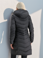 Femme portant un manteau d'hiver noir matelassé avec capuche, vue de dos, contre un mur blanc. Mode hiver, vêtement chaud, style urbain.