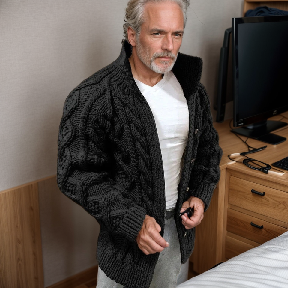 Homme mature portant un pull en laine épais gris foncé, debout dans une chambre moderne. Mode masculine, style hivernal, confort.