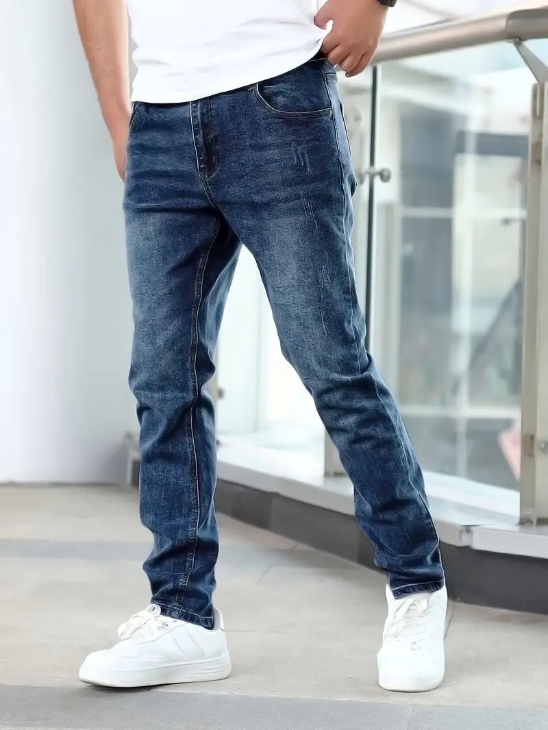 Jeans slim fit bleu délavé pour homme, associés à des baskets blanches, mode décontractée moderne, style urbain tendance.