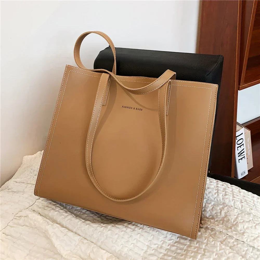 Sac à main en cuir beige élégant sur un lit, design minimaliste, poignées longues, idéal pour mode féminine, accessoire tendance et chic.