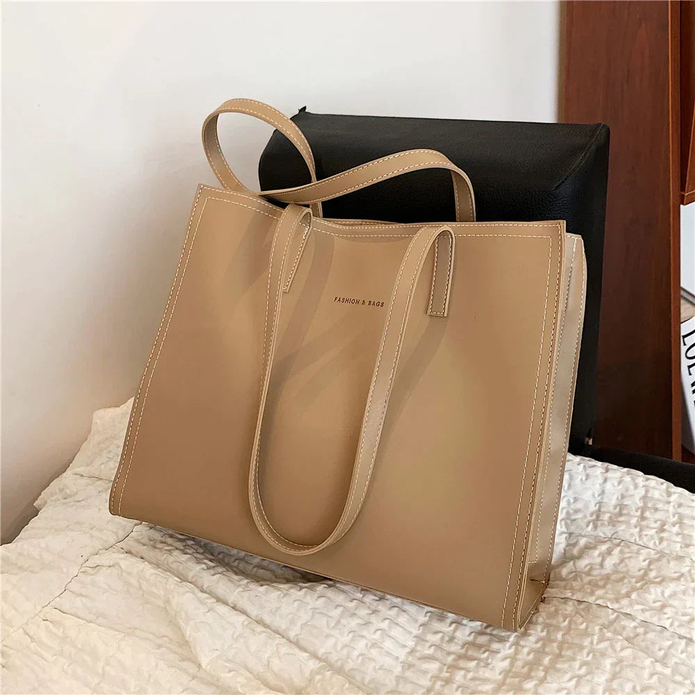 Sac à main beige élégant en cuir, posé sur un lit blanc, avec des anses longues. Accessoire mode femme, tendance et chic.