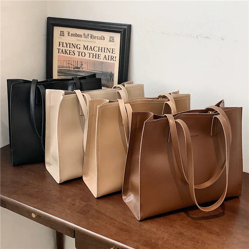 Quatre sacs à main en cuir élégants de différentes couleurs (noir, beige, marron) posés sur une table en bois, avec un cadre en arrière-plan.