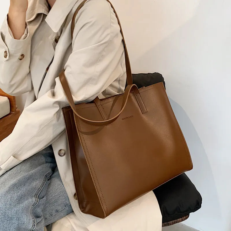 Sac à main en cuir marron porté par une personne en manteau beige et jean. Accessoire mode élégant, tendance automne, style chic et moderne.
