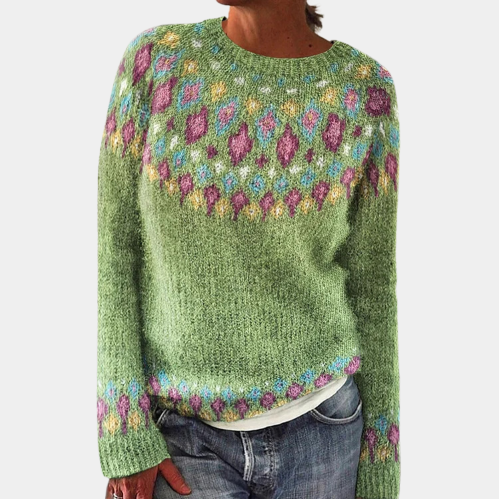 Pull vert en laine avec motifs colorés géométriques, manches longues, col rond, porté par une personne en jean. Mode automne-hiver tendance.