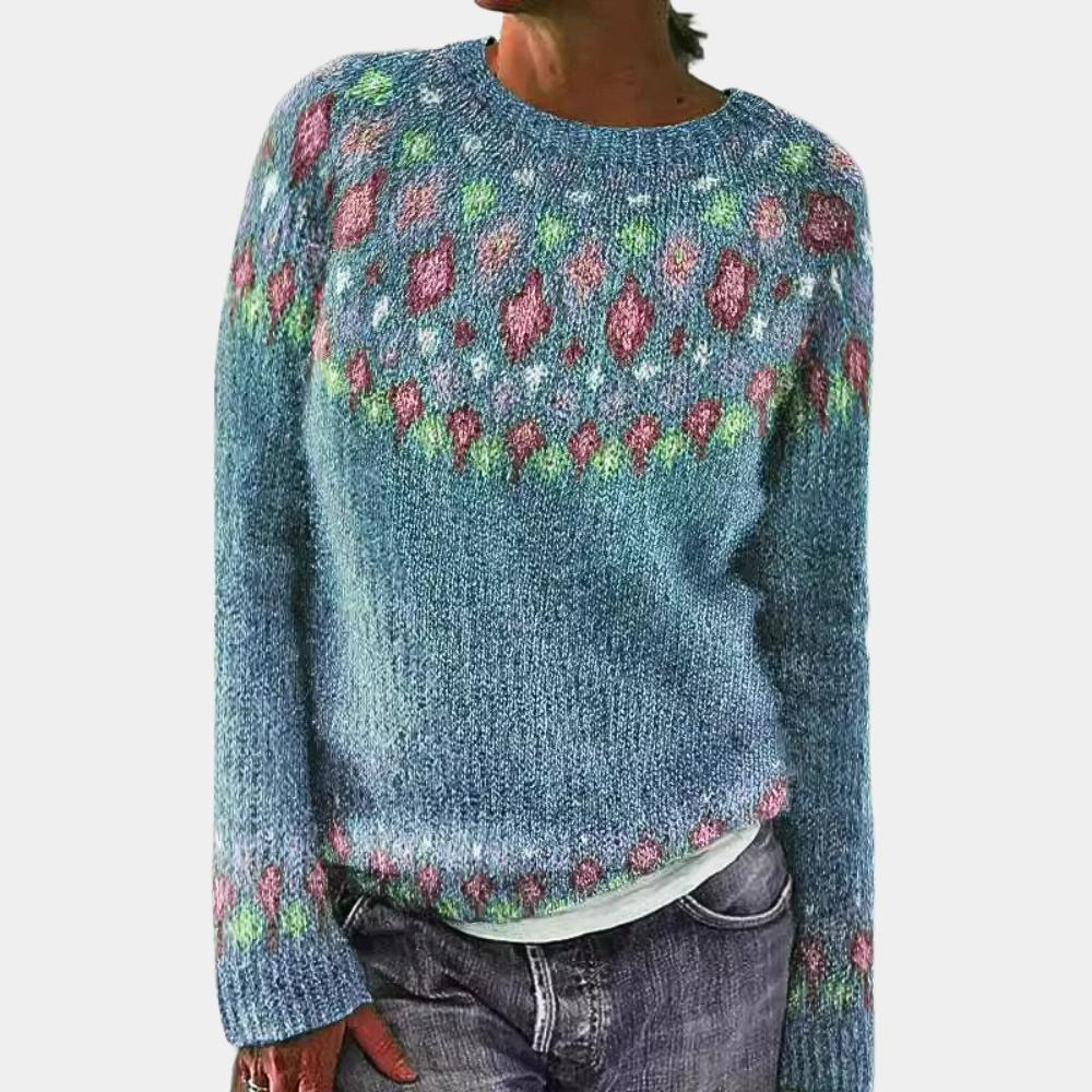 Pull en laine bleu avec motifs colorés géométriques, manches longues, col rond, porté par une personne. Mode automne-hiver, style décontracté.