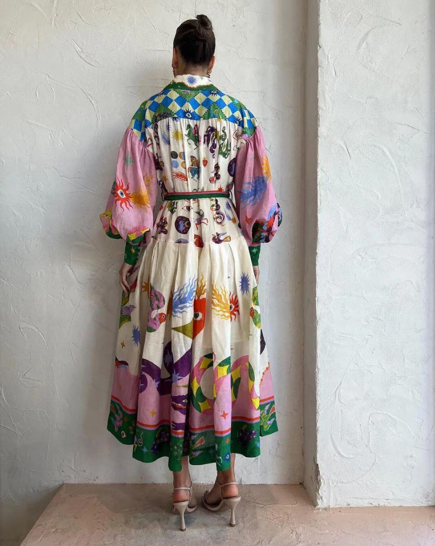 Robe bohème colorée avec motifs géométriques et floraux, manches bouffantes, ceinture à la taille, femme de dos, mur texturé blanc.