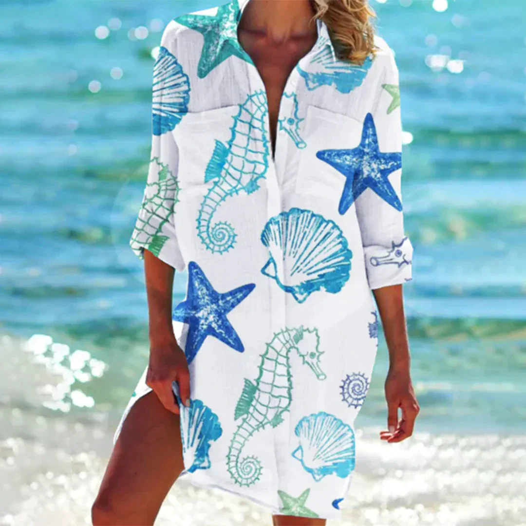Robe de plage blanche avec motifs marins bleus et verts, étoiles de mer, hippocampes et coquillages, idéale pour l'été en bord de mer.