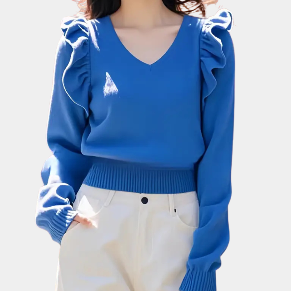 Femme portant un pull bleu à volants avec col en V, manches longues, associé à un pantalon blanc. Mode féminine élégante et moderne.