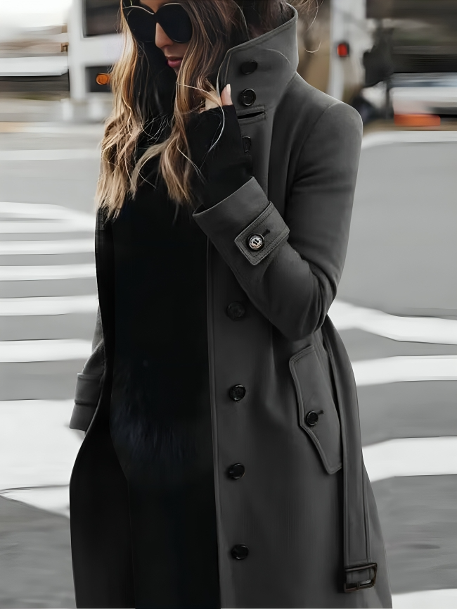 Femme élégante en manteau gris, lunettes de soleil, traversant la rue. Mode urbaine chic, style automne-hiver, tendance vestimentaire moderne.