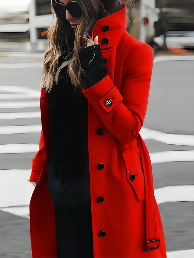 Femme portant un manteau rouge élégant avec boutons noirs, lunettes de soleil, et gants noirs, traversant une rue urbaine. Mode hiver chic.