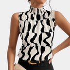 Femme portant un haut sans manches à motifs noir et blanc, col montant plissé, tenant un sac beige. Mode élégante et moderne.