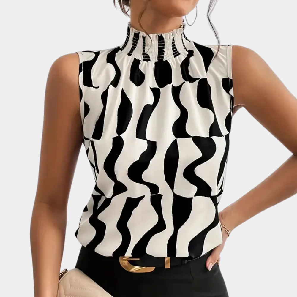 Femme portant un haut sans manches à motifs noir et blanc, col montant plissé, tenant un sac beige. Mode élégante et moderne.