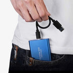 Homme tenant un SSD portable bleu avec câble USB, sortant d'une poche de jean. Disque dur externe, stockage rapide, technologie moderne.
