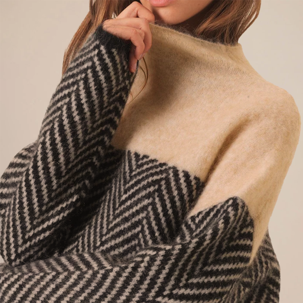 Femme portant un pull en laine à col roulé, motif chevrons noir et beige, mode automne-hiver, style élégant et confortable.