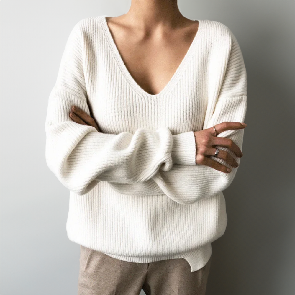 Femme portant un pull blanc en maille avec col en V, bras croisés, bague visible. Mode automne-hiver, style décontracté et élégant.