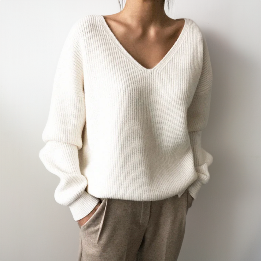 Femme portant un pull en maille blanc à col en V, manches longues, avec un pantalon beige. Mode automne-hiver, style décontracté et élégant.