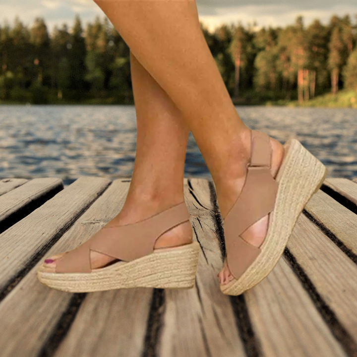 Sandales compensées beiges en cuir sur un quai en bois, bord de lac en arrière-plan, style estival, chaussures tendance pour femmes.