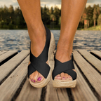 Sandales compensées noires en cuir sur un quai en bois, lac en arrière-plan. Chaussures d'été élégantes, mode féminine, confort et style.