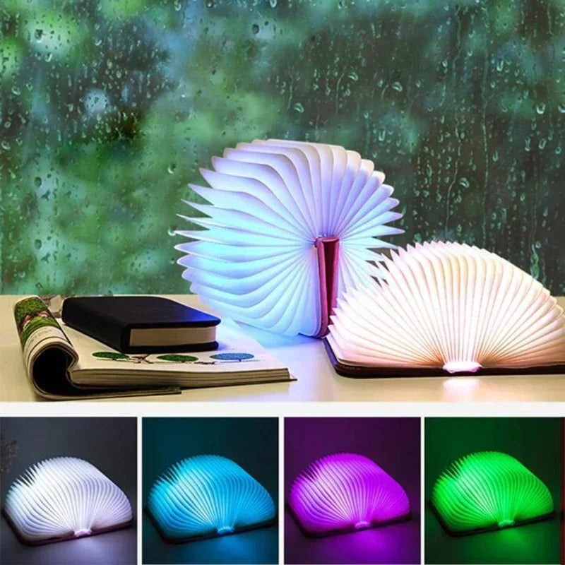 Livre lumineux LED en forme d'éventail, éclairé en blanc, bleu, violet et vert, posé sur une table devant une fenêtre avec pluie. Accessoire déco moderne.