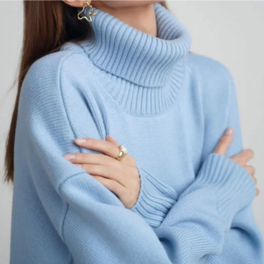 Femme portant un pull bleu col roulé, bras croisés, avec boucles d'oreilles étoile et bague dorée. Mode hiver, style élégant et confortable.