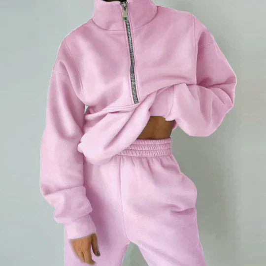 Personne portant un ensemble de survêtement rose pastel avec fermeture éclair, style décontracté et tendance, mode féminine confortable.