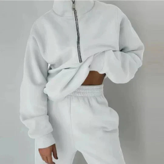 Personne portant un ensemble de survêtement blanc, composé d'un sweat à fermeture éclair et d'un pantalon assorti, style décontracté et moderne.