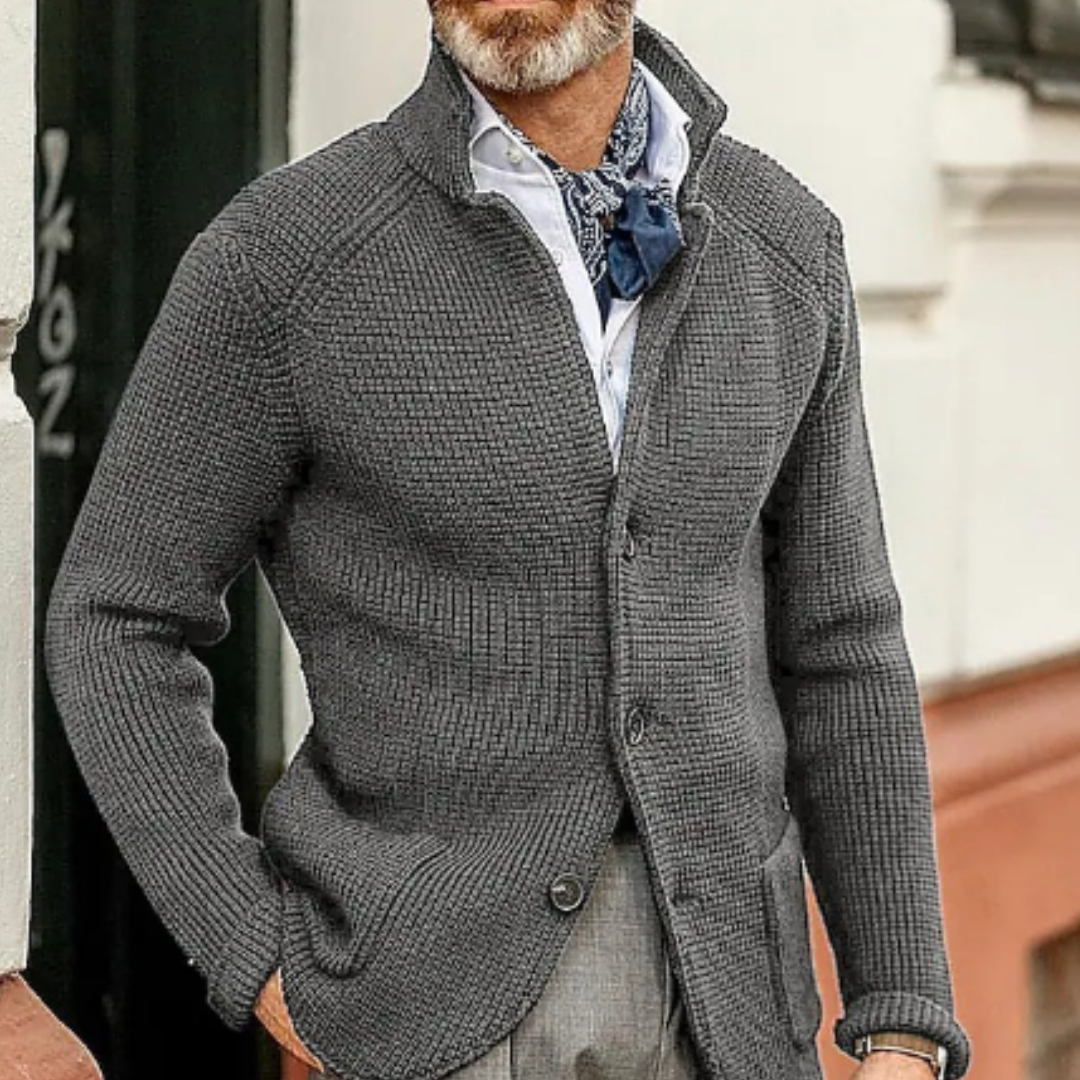 Homme portant un cardigan gris texturé, chemise blanche et foulard bleu. Mode masculine élégante, tenue automne-hiver, style urbain chic.