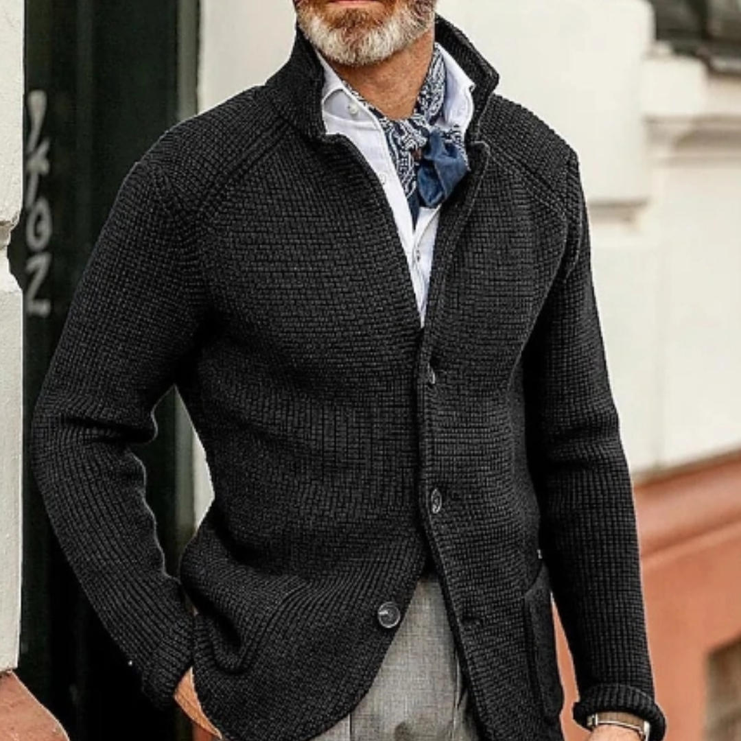 Homme portant un cardigan noir texturé, chemise blanche et foulard bleu, style élégant et moderne, mode masculine automne-hiver.