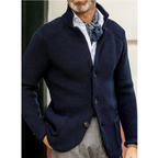 Homme portant un cardigan bleu marine texturé, chemise blanche et foulard élégant. Mode masculine chic, tenue automne-hiver tendance.
