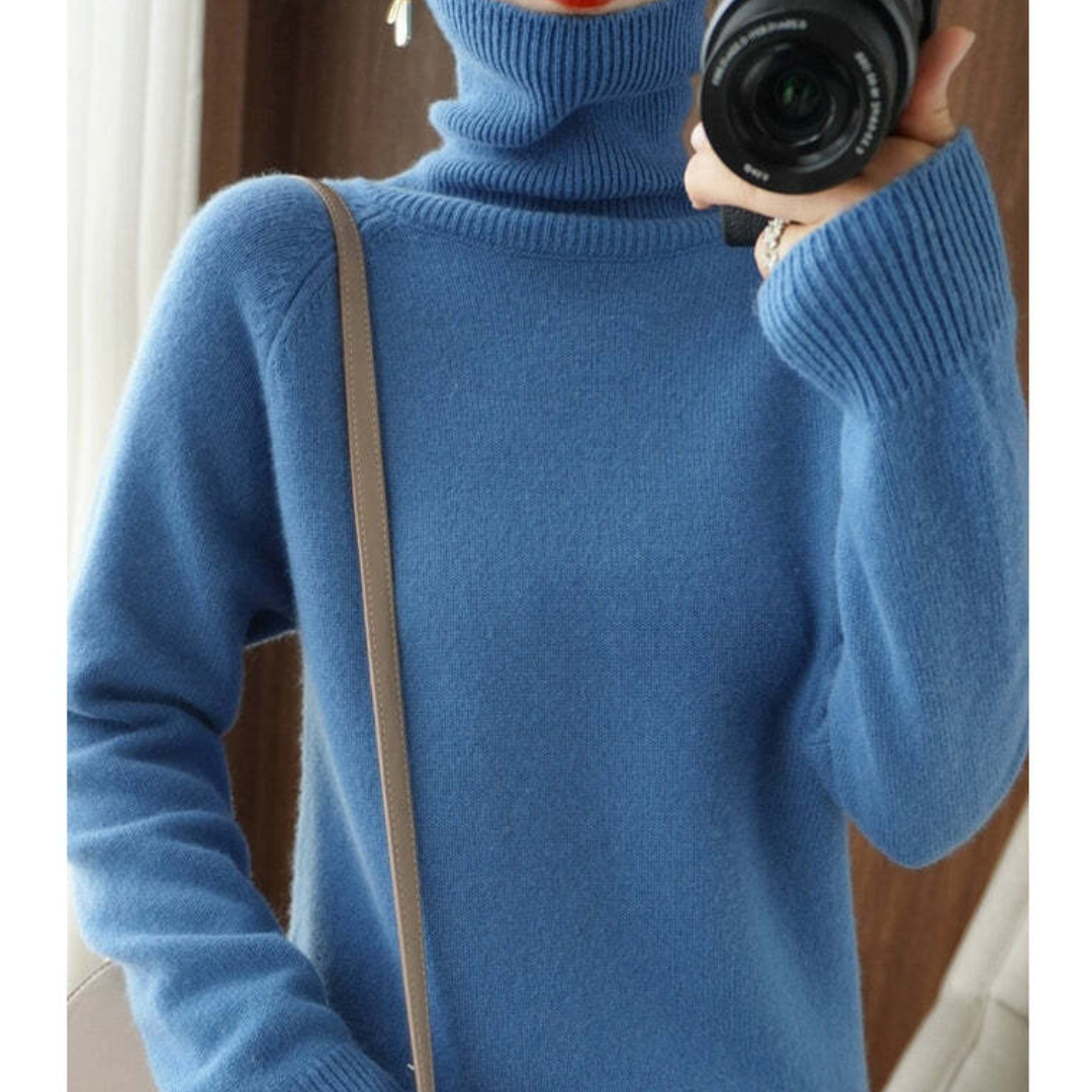 Pull bleu col roulé en laine, manches longues, porté par une personne tenant un appareil photo. Mode hiver, vêtement chaud et confortable.