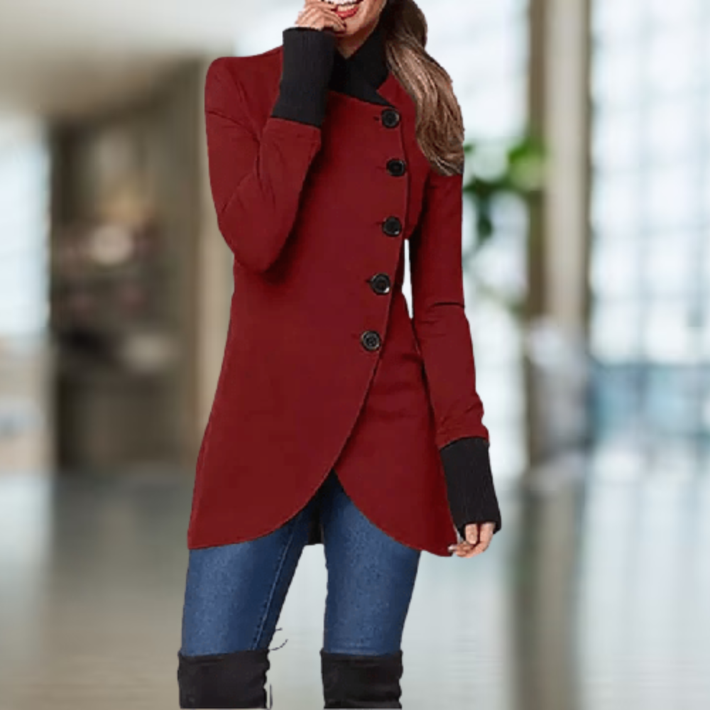 Femme portant un manteau rouge élégant avec boutons noirs, col montant, manches longues, sur fond flou intérieur. Mode automne-hiver chic.